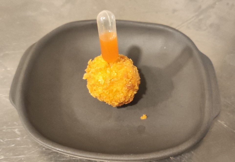 Lautasella on kroketti joka on päällystetty kuivatulla maissilla ja jonka keskellä on maustenestettä sisältävä putkilo.